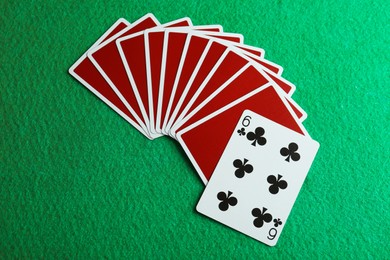 Playing cards and six of clubs on green table, flat lay