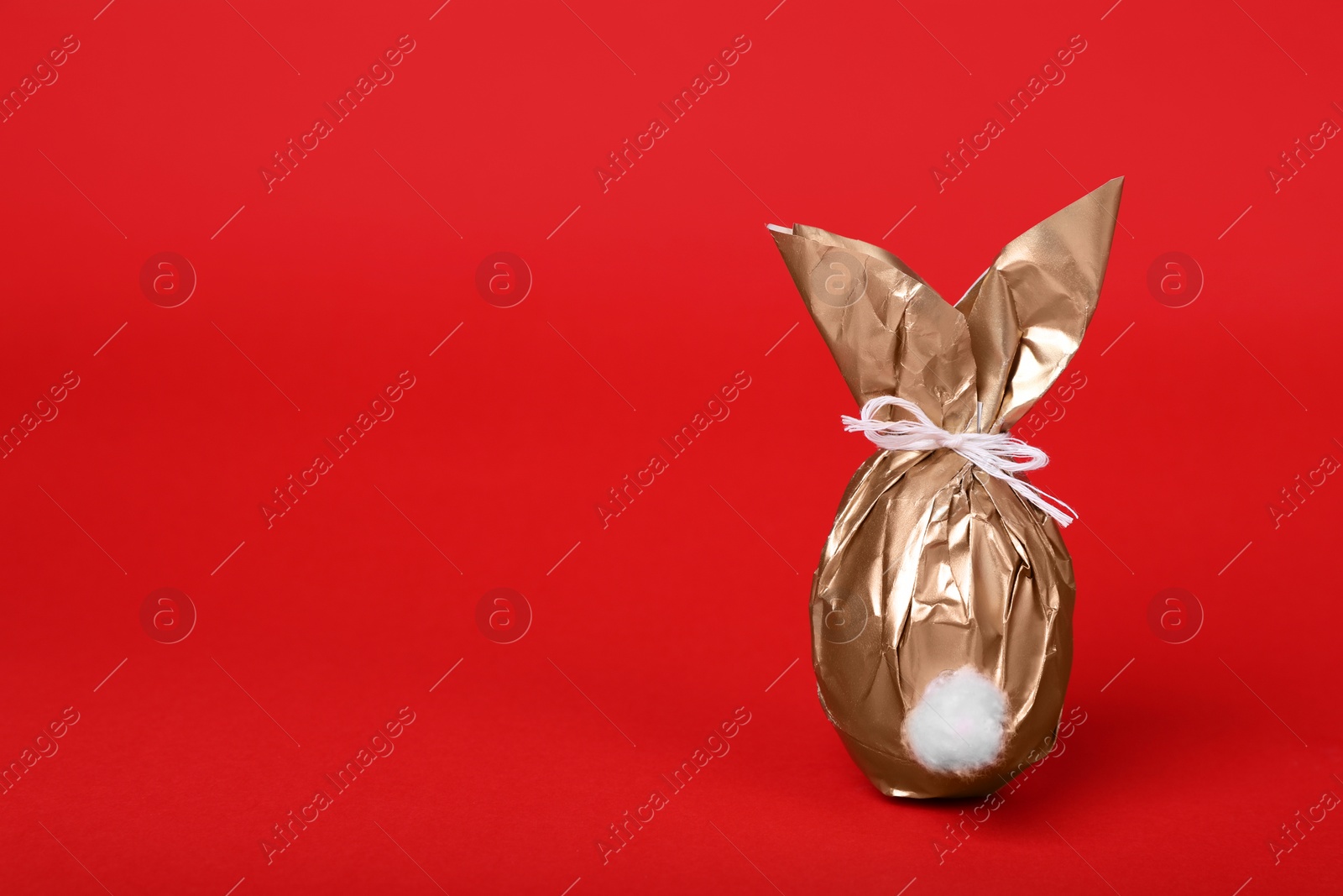 Photo of Easter bunny made of shiny gold paper and egg on red background. Space for text