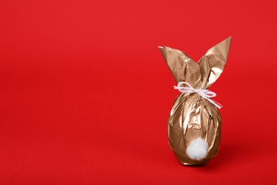 Photo of Easter bunny made of shiny gold paper and egg on red background. Space for text