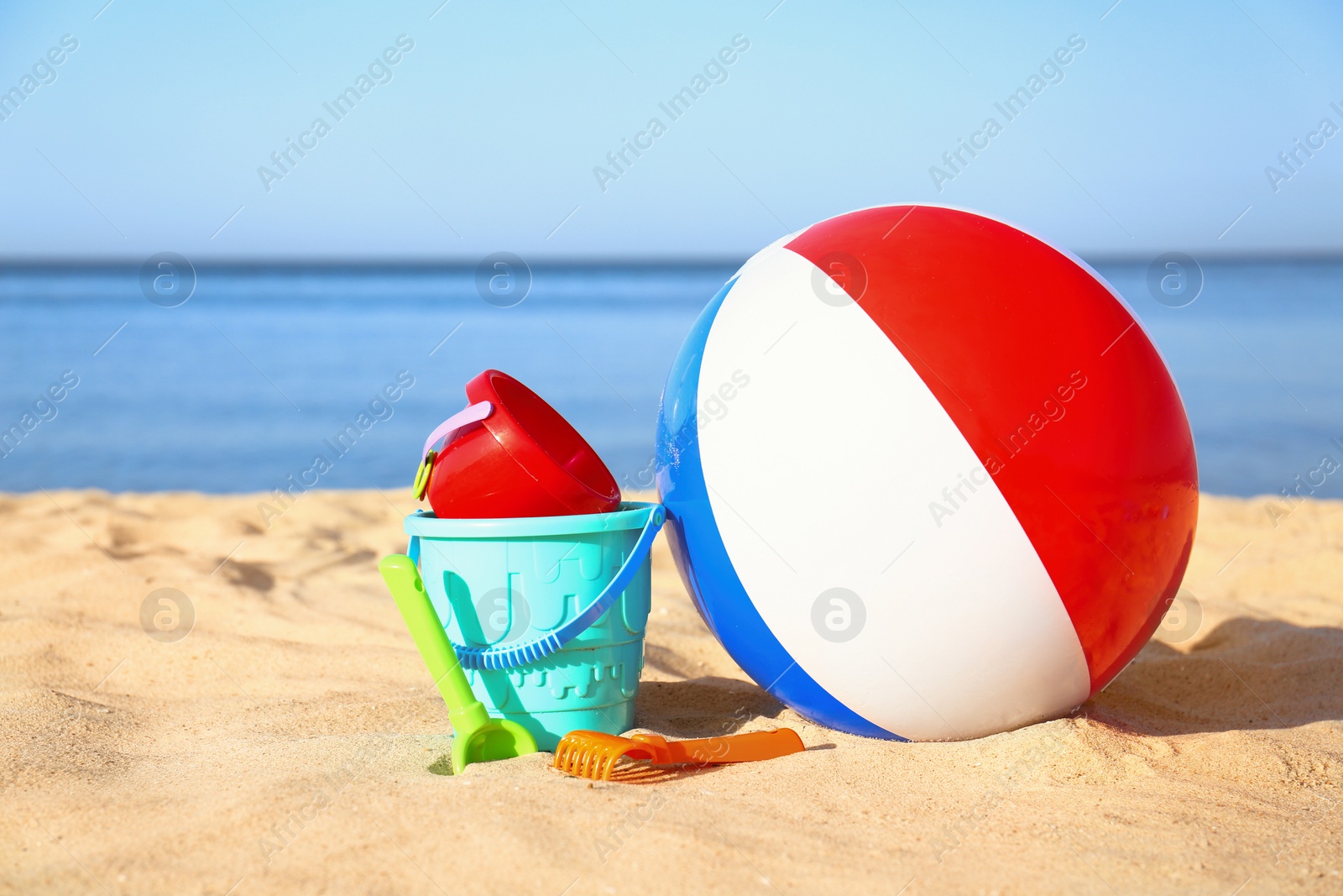 Photo of Set of plastic beach toys and colorful ball on sand near sea. Space for text