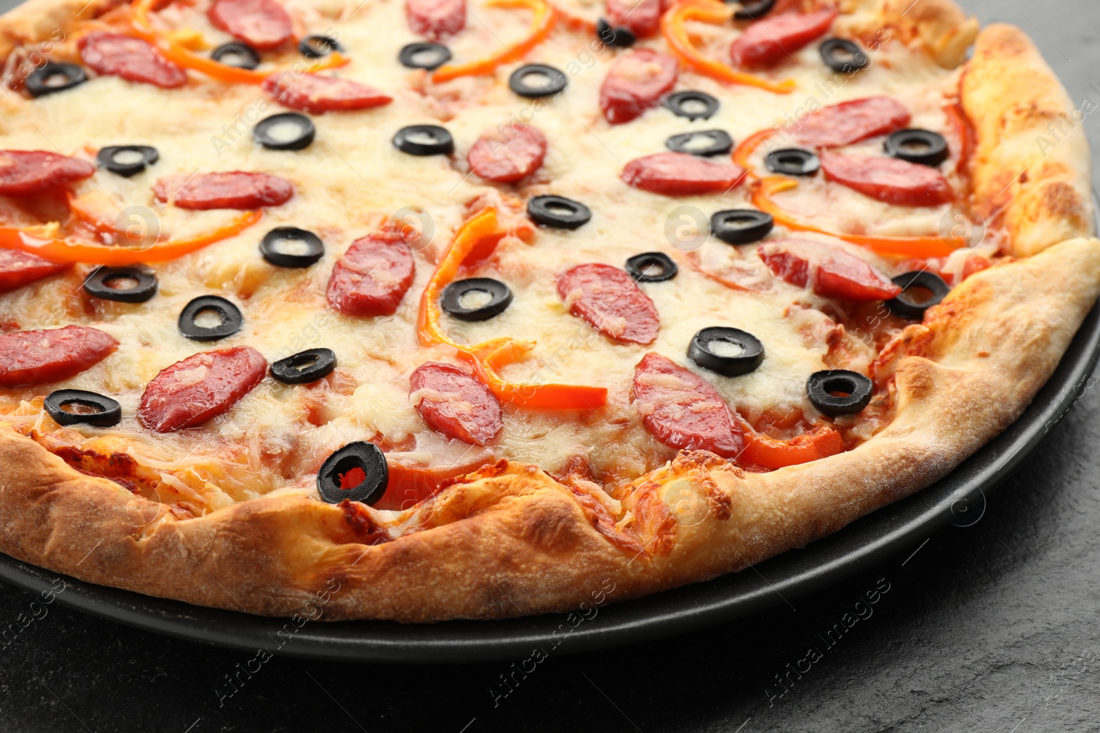 Photo of Tasty pizza with cheese, dry smoked sausages, olives and pepper on grey table, closeup