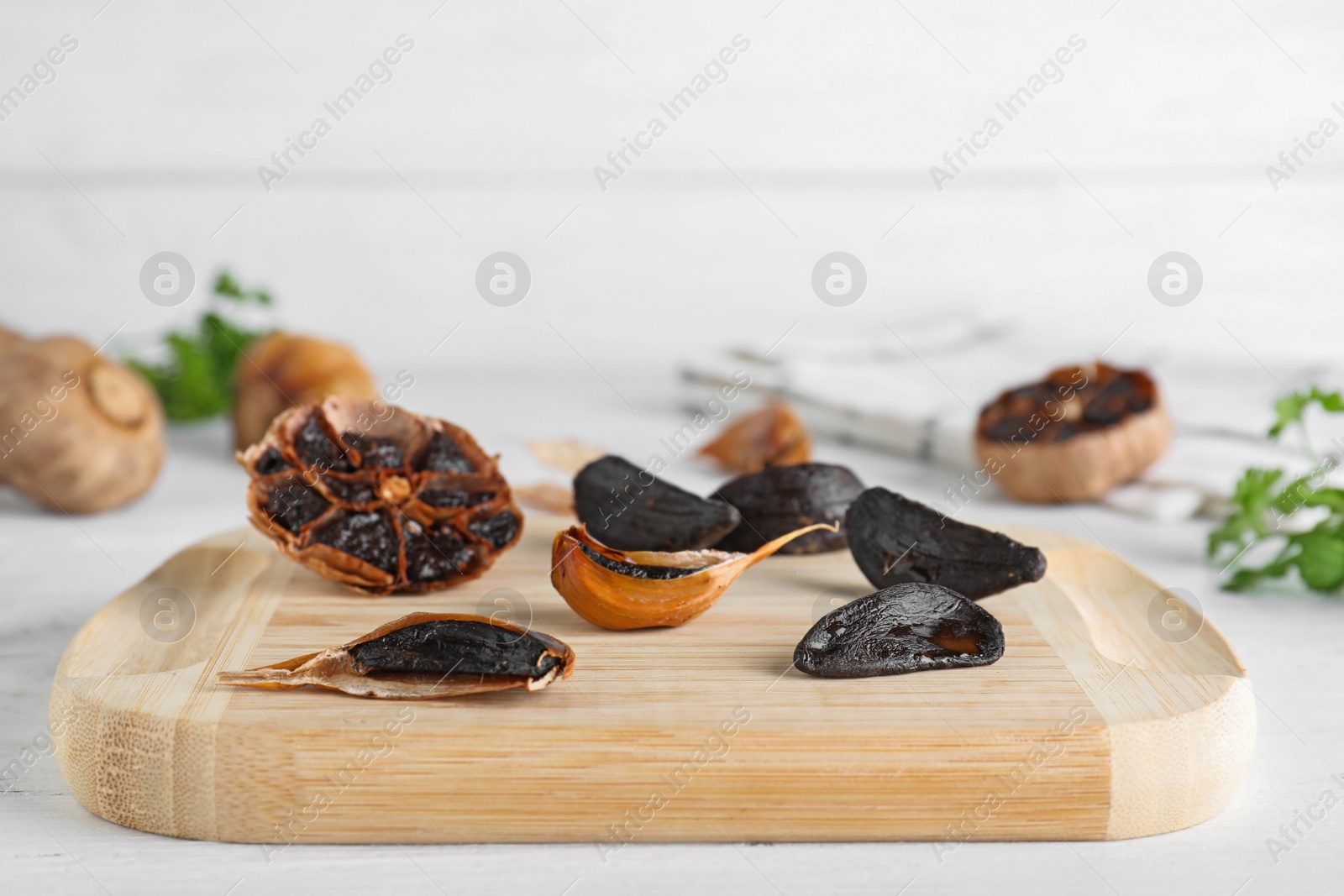 Photo of Wooden board with black garlic on white table