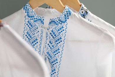 Photo of Beautiful shirts with different embroidery designs hanging on grey background, closeup. Ukrainian national clothes