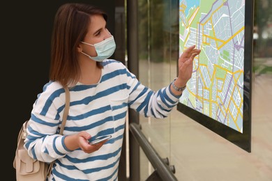 Image of Young woman in medical face mask near public transport map at bus stop