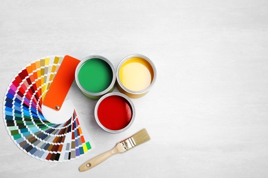 Photo of Cans with paint, brush and color palette on light background, top view. Space for text