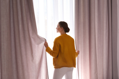 Woman opening window curtains at home in morning