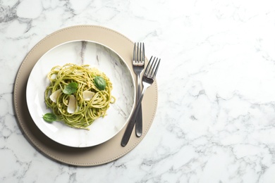 Flat lay composition with plate of delicious basil pesto pasta and space for text on marble table