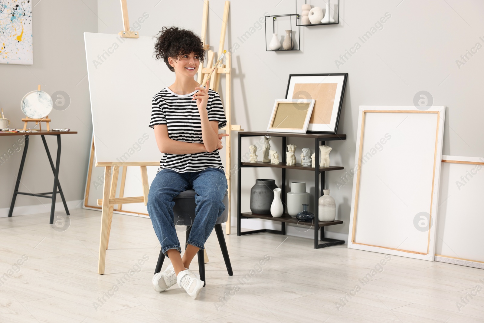 Photo of Young woman with brush palette near easel in studio