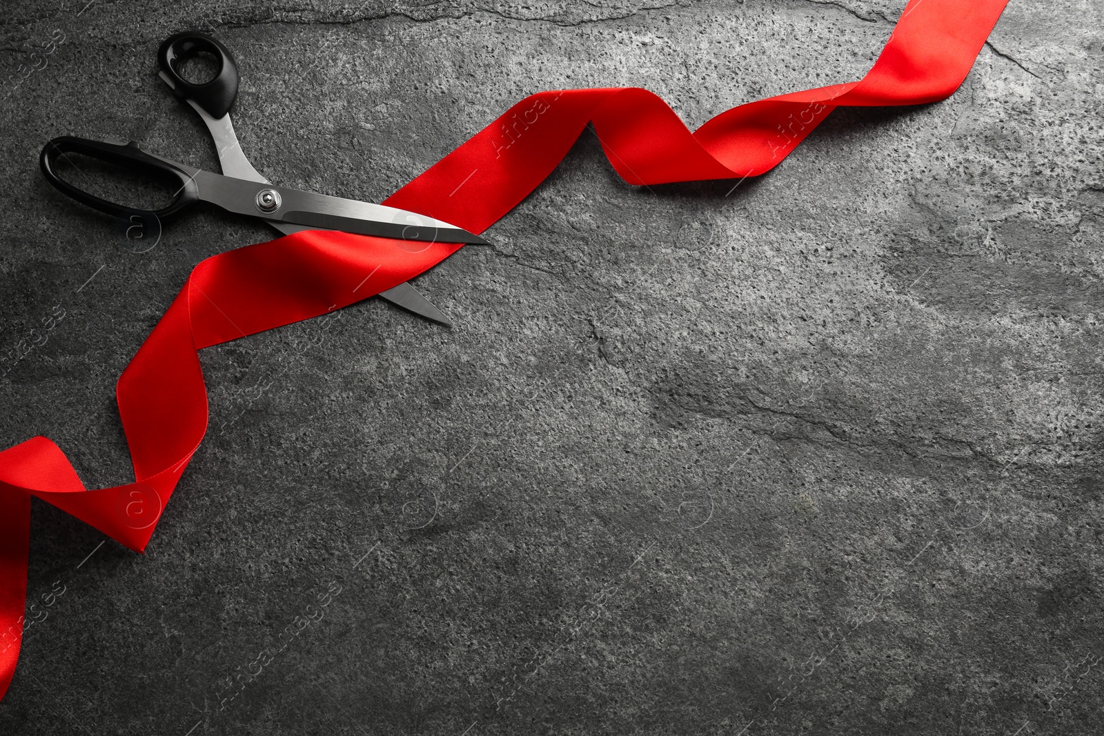 Photo of Red ribbon and scissors on dark grey background, top view. Space for text