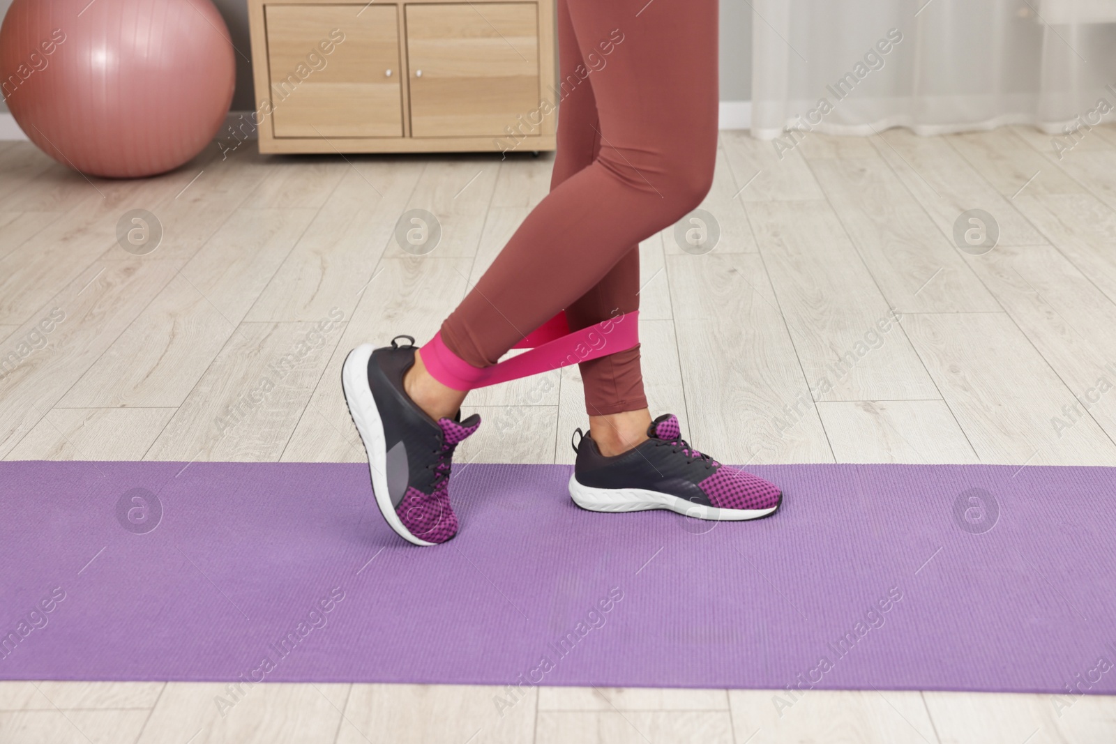 Photo of Online fitness trainer. Woman doing exercise with elastic band near laptop at home, closeup