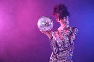 Photo of Beautiful young woman with disco ball posing on color background in neon lights. Space for text
