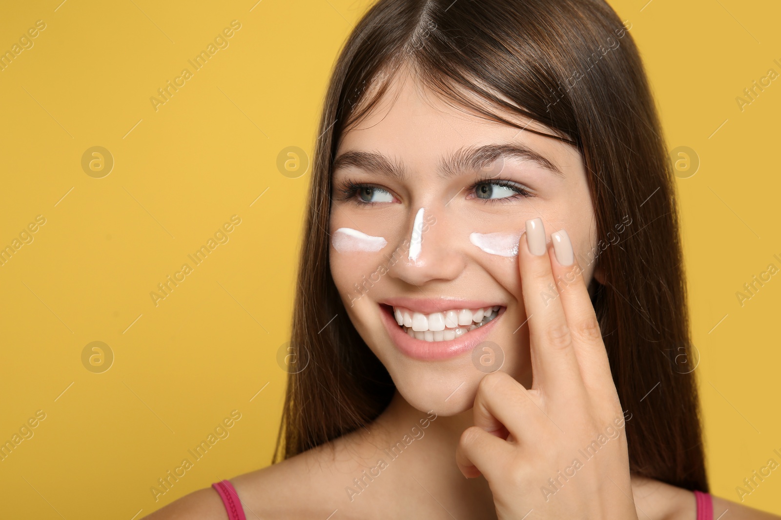 Photo of Teenage girl applying sun protection cream on her face against yellow background