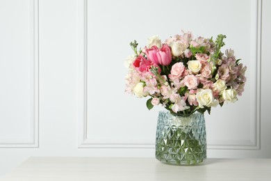 Photo of Beautiful bouquet of fresh flowers in vase on table near white wall. Space for text