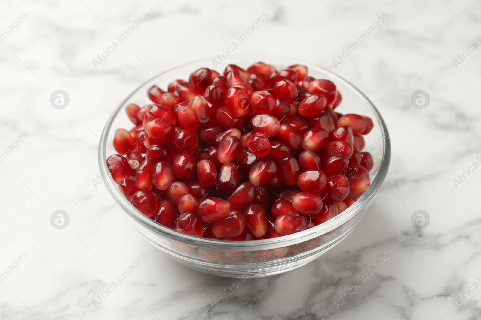 Photo of Ripe juicy pomegranate grains in bowl on white marble table, closeup