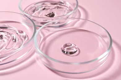 Photo of Petri dishes with liquids on pale pink background, closeup