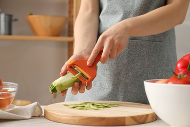 Photo of Woman peeling fresh zucchini at table in kitchen, closeup