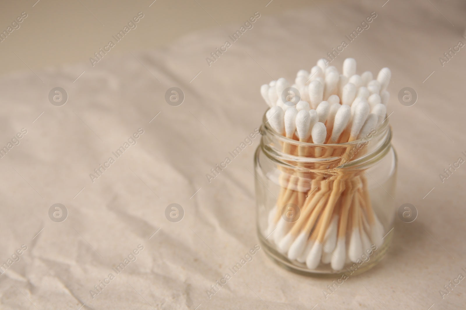 Photo of Jar of clean cotton buds on crumpled paper. Space for text