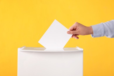 Photo of Woman putting her vote into ballot box on orange background, closeup