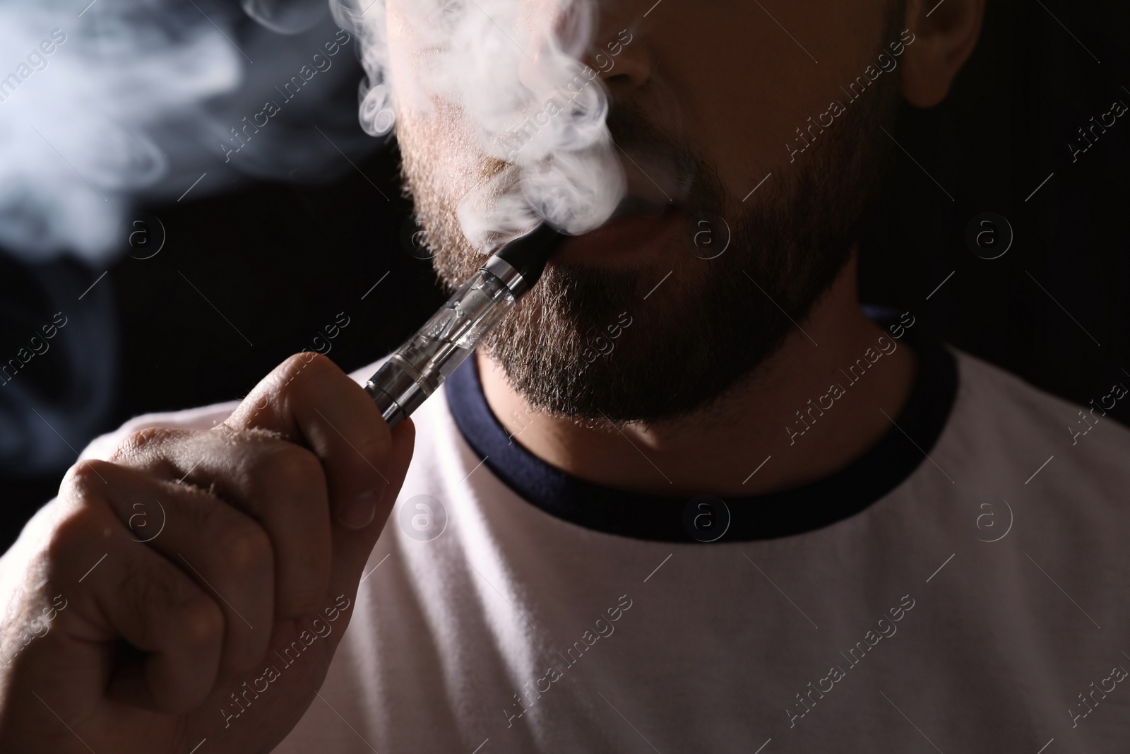 Photo of Man using electronic cigarette on black background, closeup