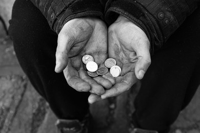 Photo of Poor homeless man holding coins outdoors, top view. Black and white effect