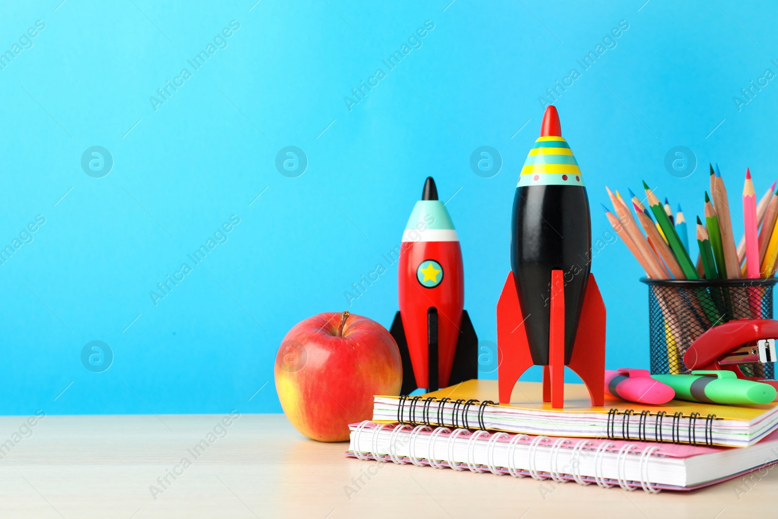 Photo of Bright toy rockets and school supplies on wooden table. Space for text