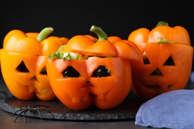 Photo of Bell peppers with black olives, mozzarella and lettuce as Halloween monsters on dark table, closeup