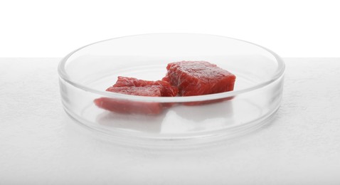 Photo of Petri dish with pieces of raw cultured meat on table against white background