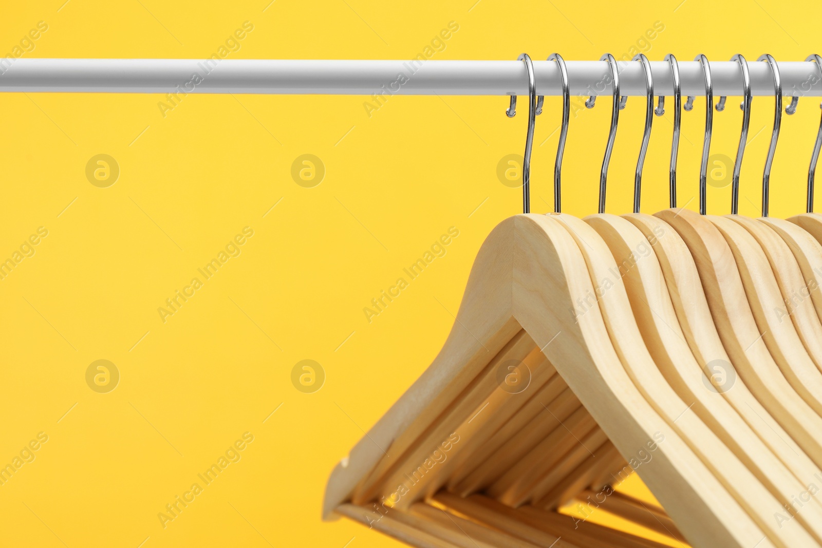 Photo of Empty clothes hangers on rack against orange background, closeup. Space for text