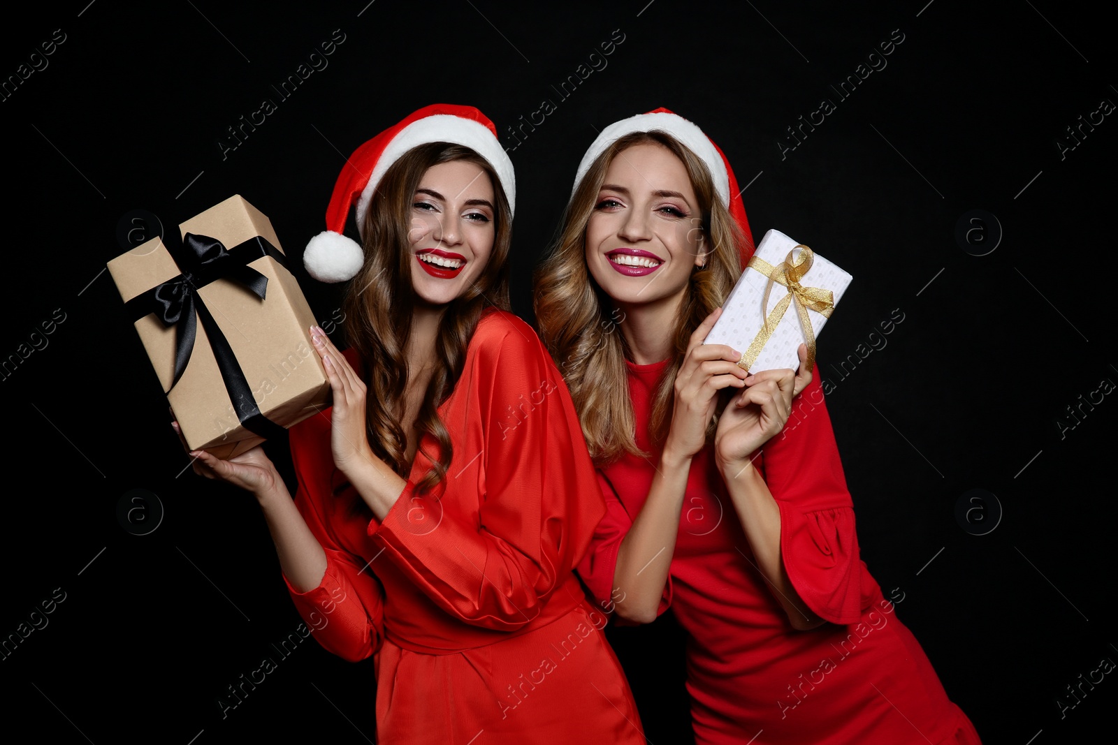 Photo of Happy women in Santa hats with gift boxes on black background. Christmas party