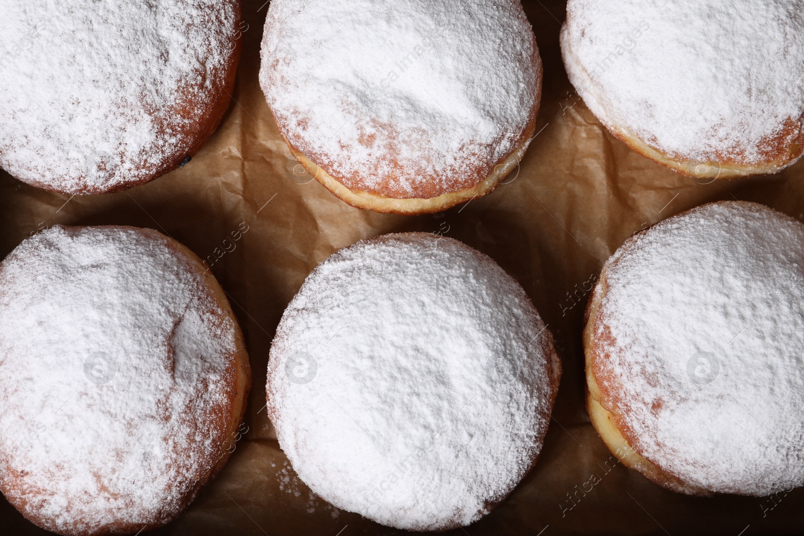 Photo of Delicious buns with powdered sugar on parchment paper, top view