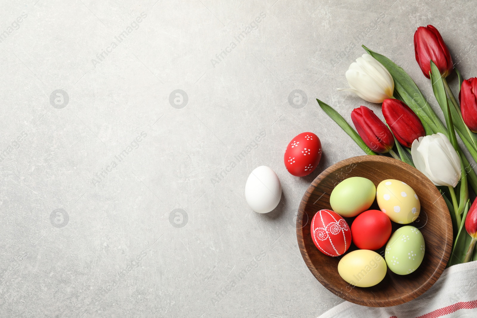 Photo of Flat lay composition of painted Easter eggs and spring flowers on light background, space for text