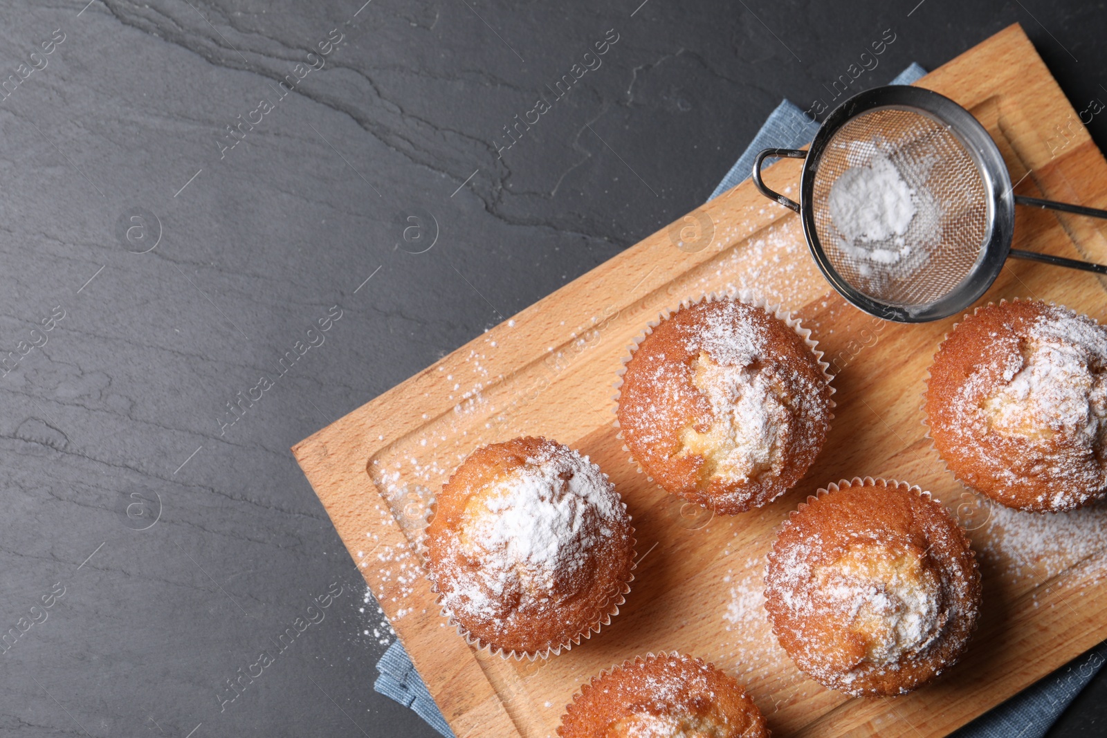 Photo of Delicious sweet muffins and sieve on black textured table, top view. Space for text