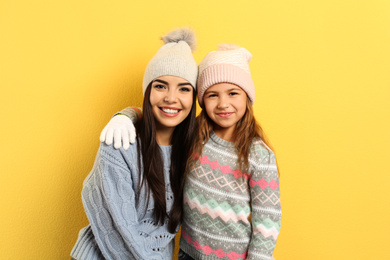 Photo of Happy mother and daughter in warm clothes on yellow background. Winter vacation