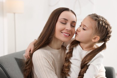 Photo of Cute daughter kissing her mom on sofa at home