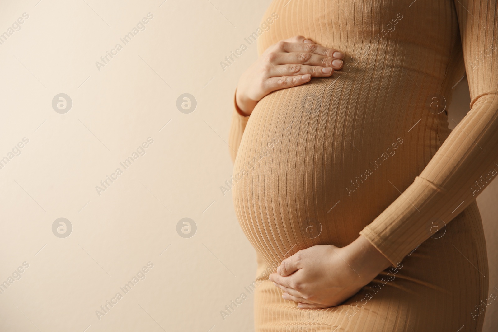 Photo of Pregnant woman touching her belly on beige background, closeup. Space for text