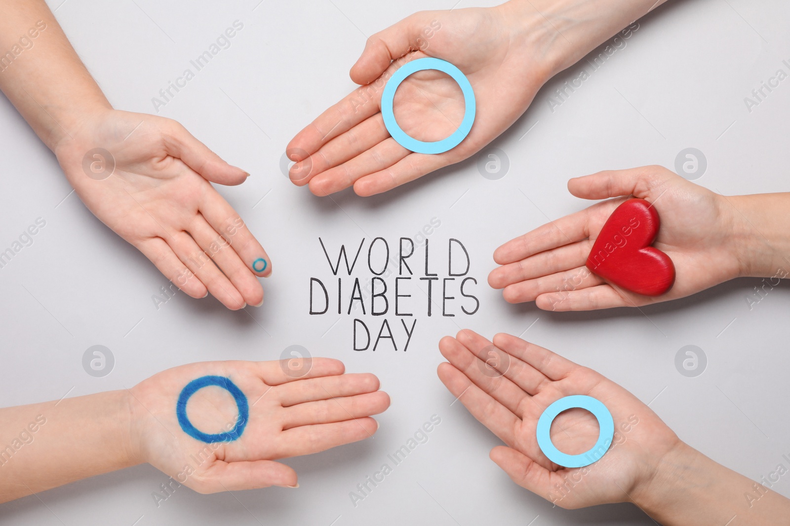 Photo of People showing blue circles and red heart near text World Diabetes Day on light background, top view