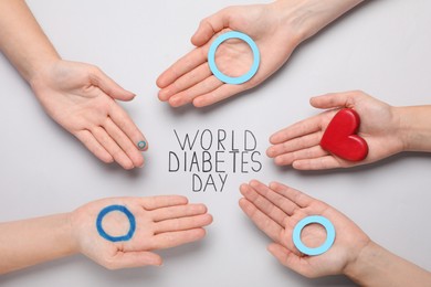 People showing blue circles and red heart near text World Diabetes Day on light background, top view