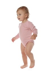 Cute baby girl in pink bodysuit learning to walk on white background