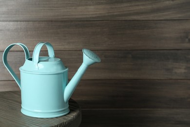 Photo of Turquoise metal watering can on table against wooden background, space for text