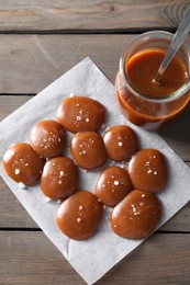 Tasty candies, caramel sauce and salt on wooden table, top view