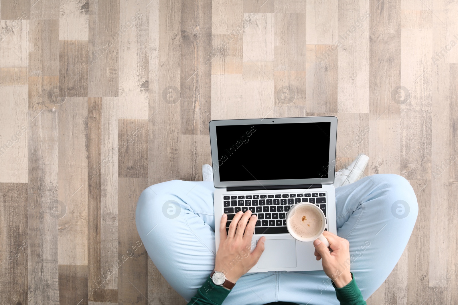 Photo of Young man with laptop and cup of coffee sitting on floor, top view