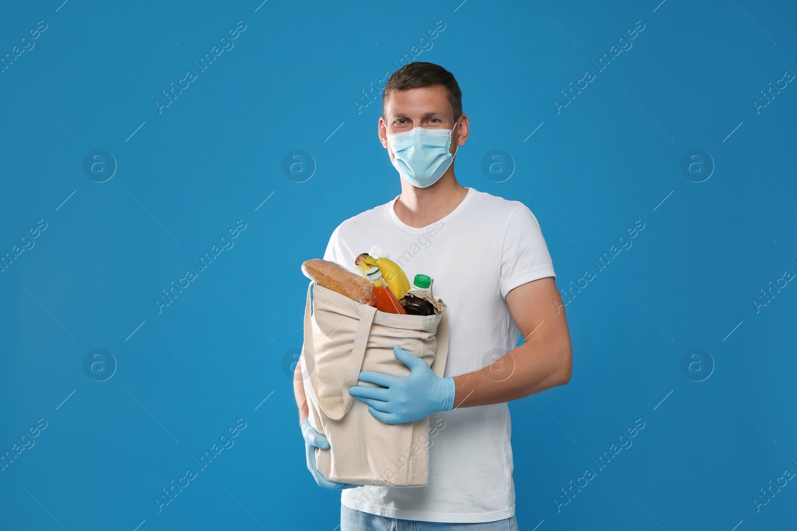 Photo of Male volunteer in protective mask and gloves with products on blue background. Aid during coronavirus quarantine	