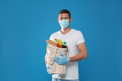 Photo of Male volunteer in protective mask and gloves with products on blue background. Aid during coronavirus quarantine	