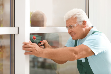 Mature construction worker repairing plastic window with electric screwdriver indoors