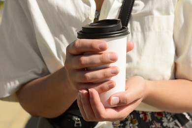 Woman holding takeaway coffee cup outdoors, closeup