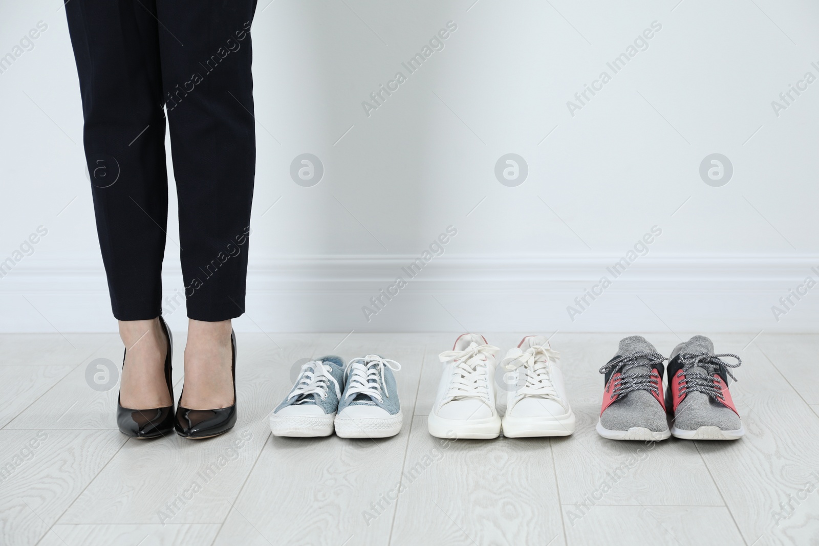 Photo of Different comfortable sneakers near businesswoman wearing high heel shoes indoors, closeup