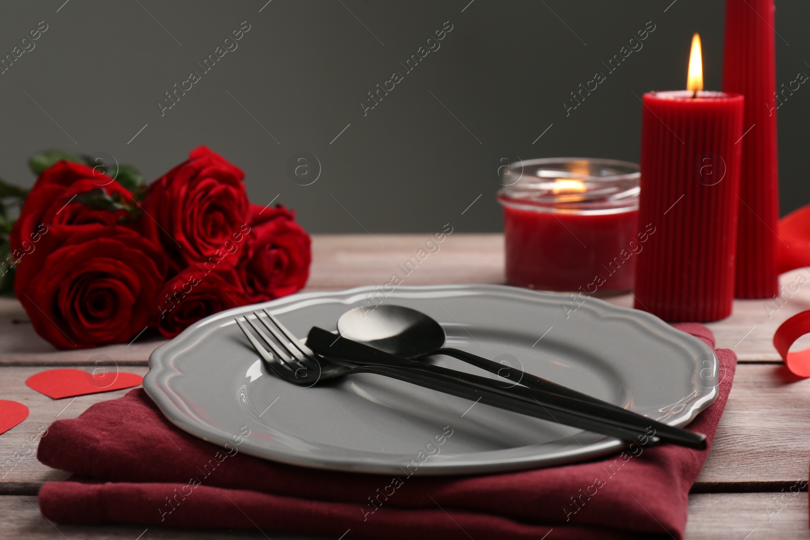 Photo of Romantic place setting with red roses and candles on wooden table. St. Valentine's day dinner