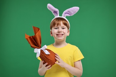 Photo of Easter celebration. Cute little boy with bunny ears and wrapped egg on green background