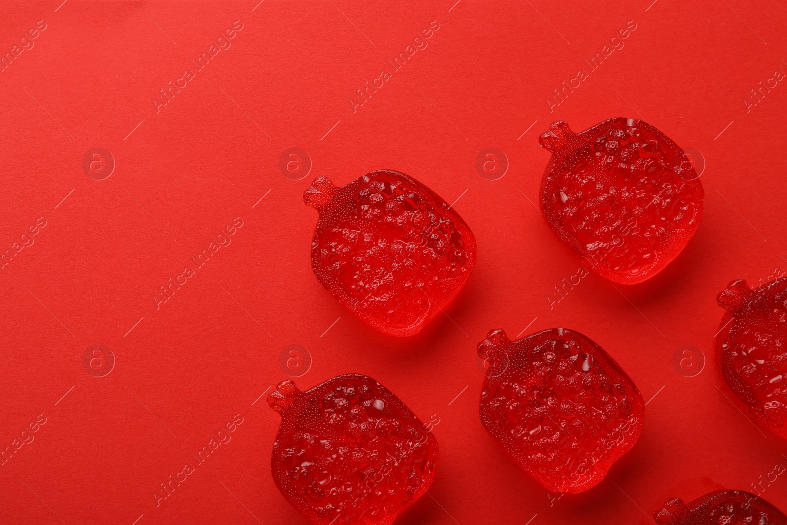 Photo of Delicious gummy pomegranate candies on red background, flat lay. Space for text