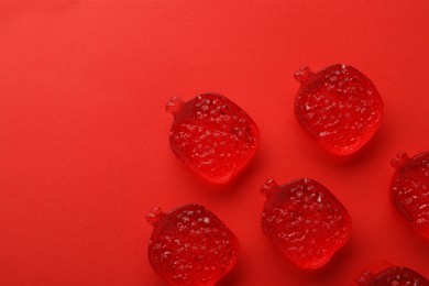 Photo of Delicious gummy pomegranate candies on red background, flat lay. Space for text